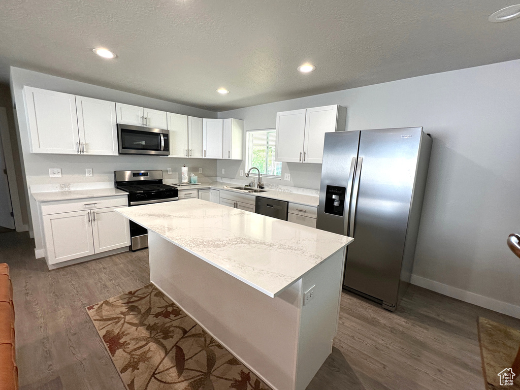 Kitchen featuring stainless steel appliances, dark wood-style floors, white cabinetry, a kitchen island, and light stone countertops