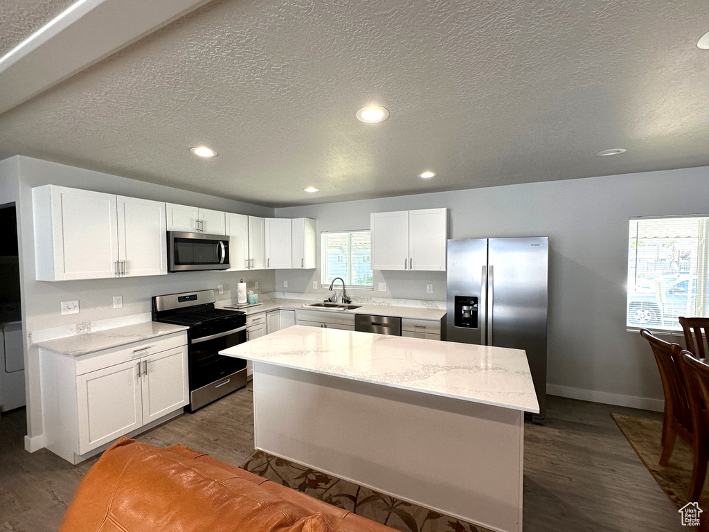 Kitchen with stainless steel appliances, dark wood finished floors, white cabinets, a kitchen island, and a textured ceiling