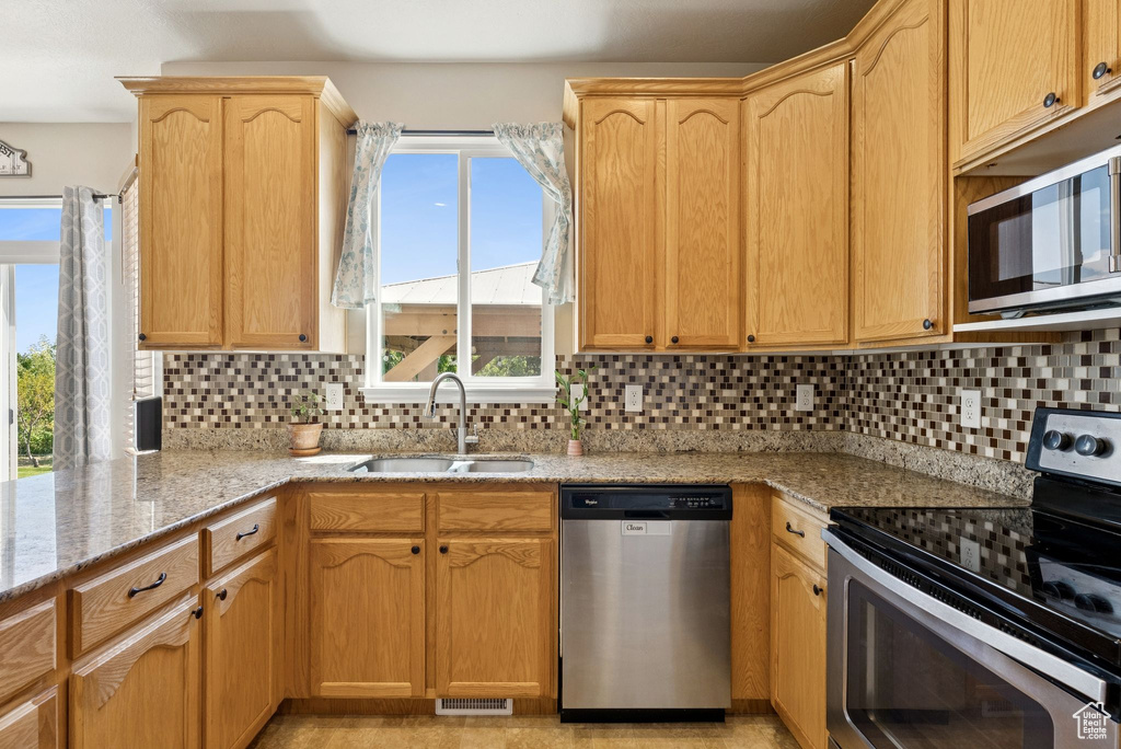 Kitchen with appliances with stainless steel finishes, light stone counters, backsplash, and light brown cabinetry