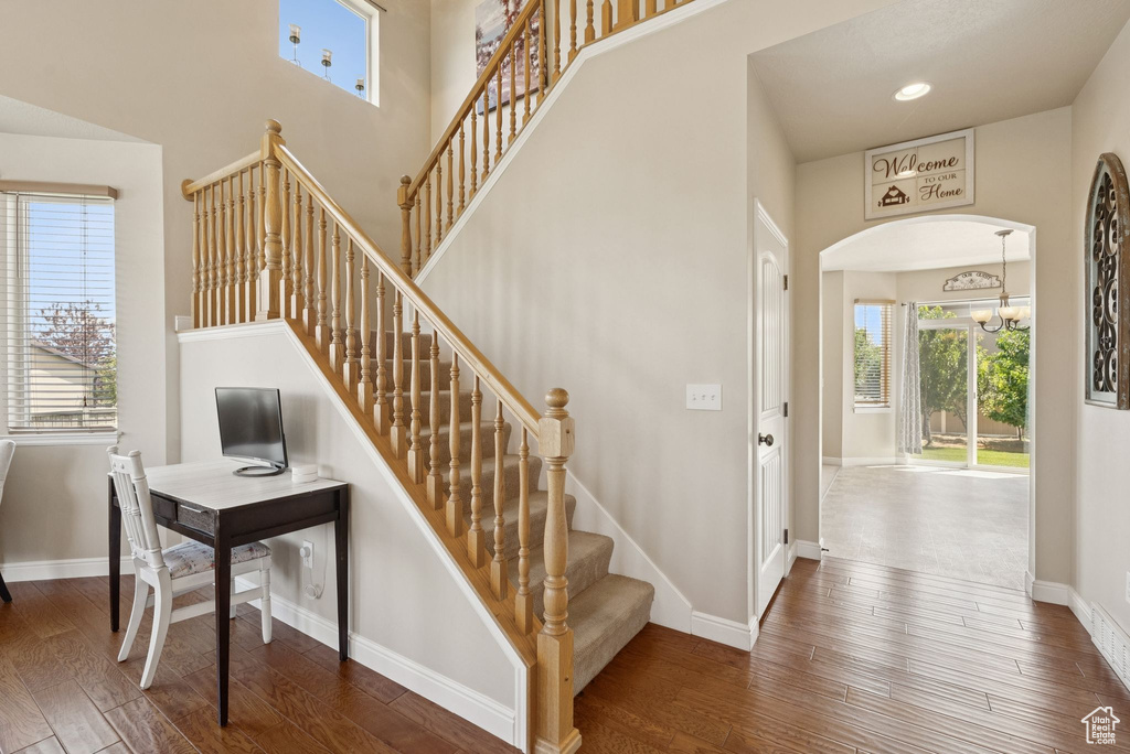 Stairway with wood finished floors, a high ceiling, arched walkways, and a chandelier