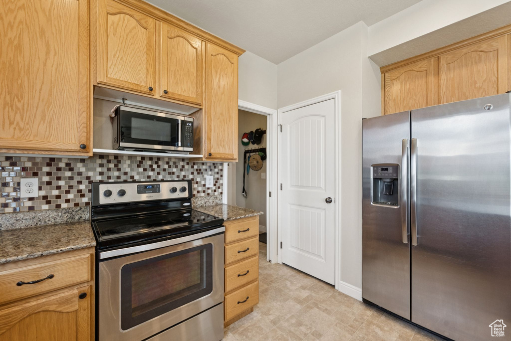 Kitchen with stainless steel appliances, tasteful backsplash, stone countertops, and light brown cabinetry