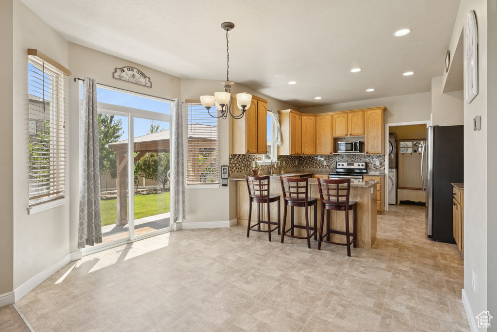 Kitchen with appliances with stainless steel finishes, a peninsula, a chandelier, tasteful backsplash, and recessed lighting