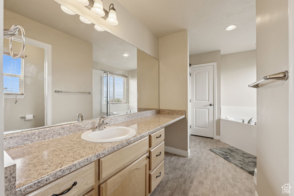 Bathroom featuring vanity, a bath, wood finished floors, and recessed lighting