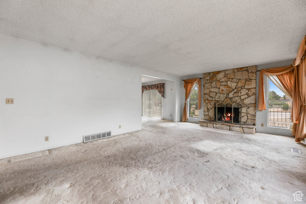 Unfurnished living room with a textured ceiling, healthy amount of natural light, a fireplace, and carpet flooring