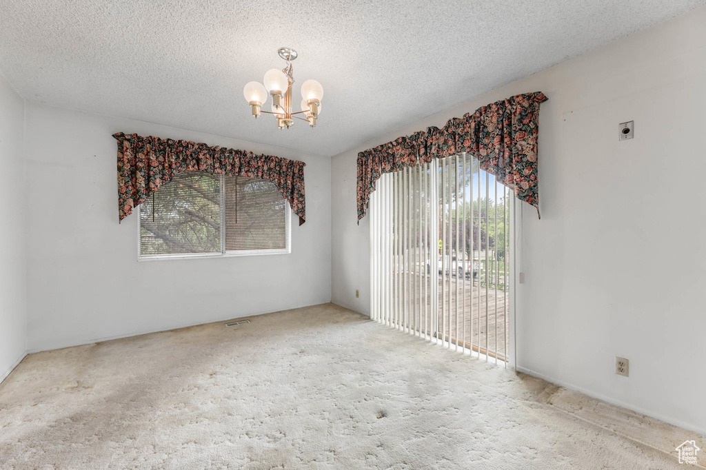 Carpeted empty room featuring a chandelier and a textured ceiling