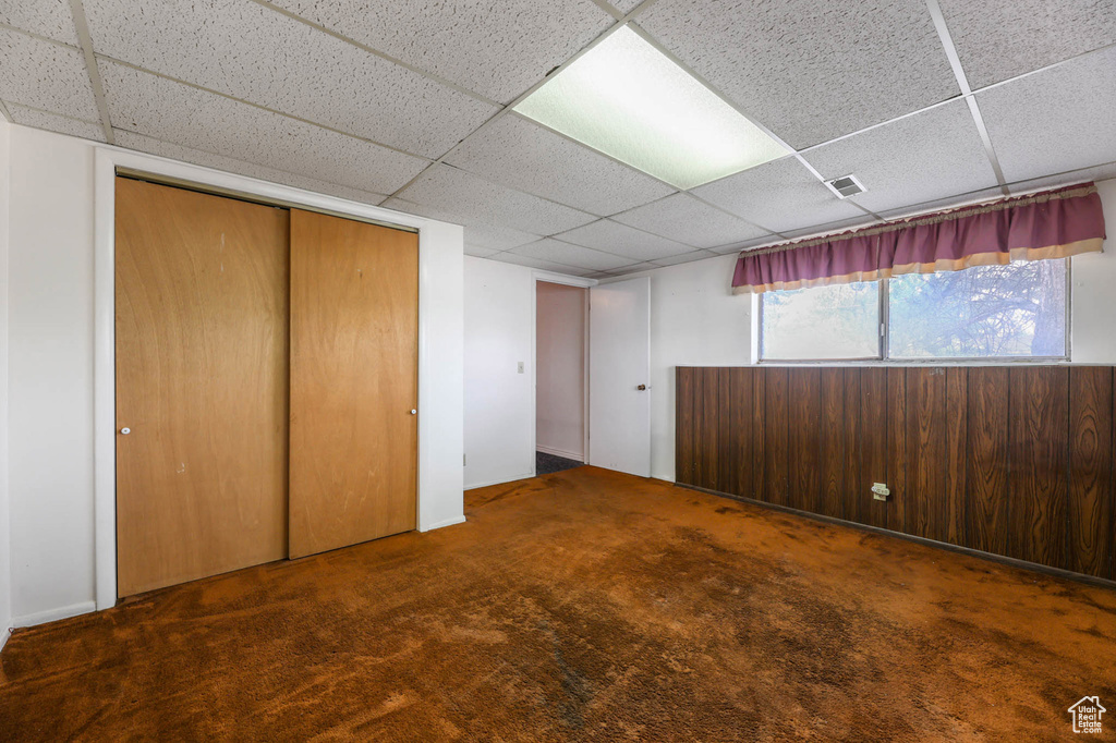 Unfurnished bedroom with a drop ceiling, a closet, and carpet