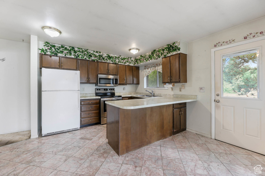 Kitchen featuring appliances with stainless steel finishes, a peninsula, light countertops, light marble finish flooring, and dark brown cabinets