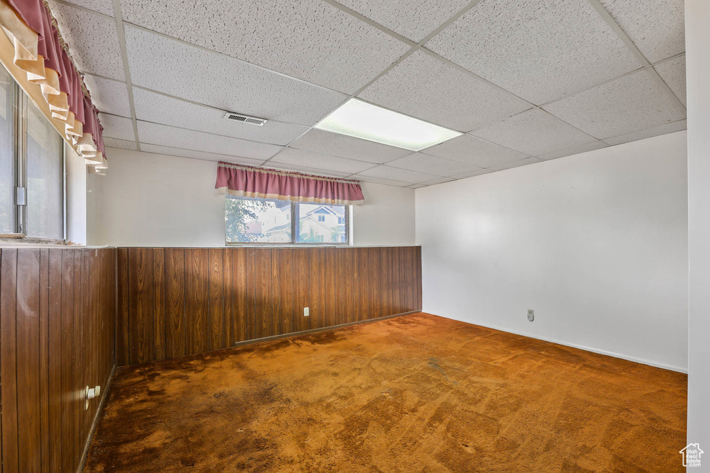 Unfurnished room featuring a paneled ceiling, wooden walls, carpet flooring, and a wainscoted wall