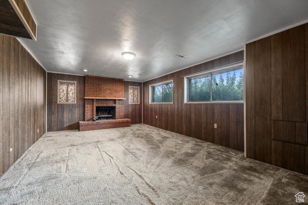 Unfurnished living room featuring carpet, wood walls, and a brick fireplace