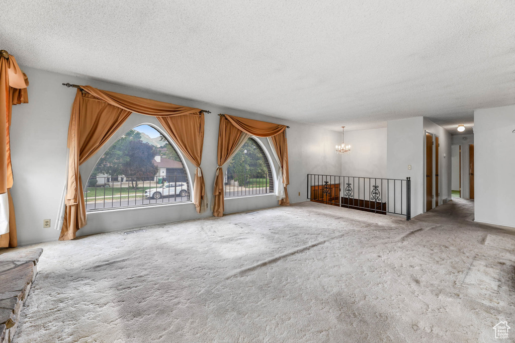 Unfurnished living room featuring a chandelier, a textured ceiling, and carpet floors