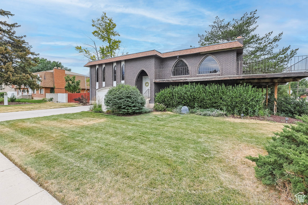 View of front of home with concrete driveway, a front yard, brick siding, and a chimney