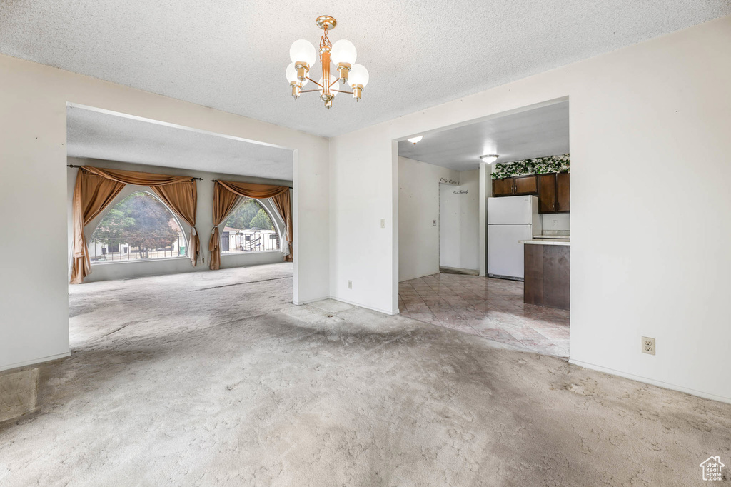 Unfurnished dining area with a chandelier, light carpet, and a textured ceiling