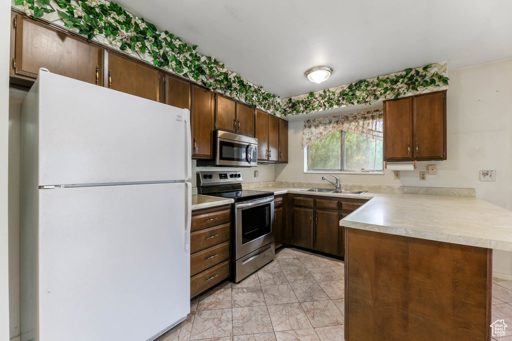 Kitchen with appliances with stainless steel finishes, a peninsula, light countertops, and light marble finish flooring