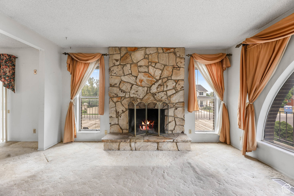 Unfurnished living room with a textured ceiling, carpet floors, and a stone fireplace