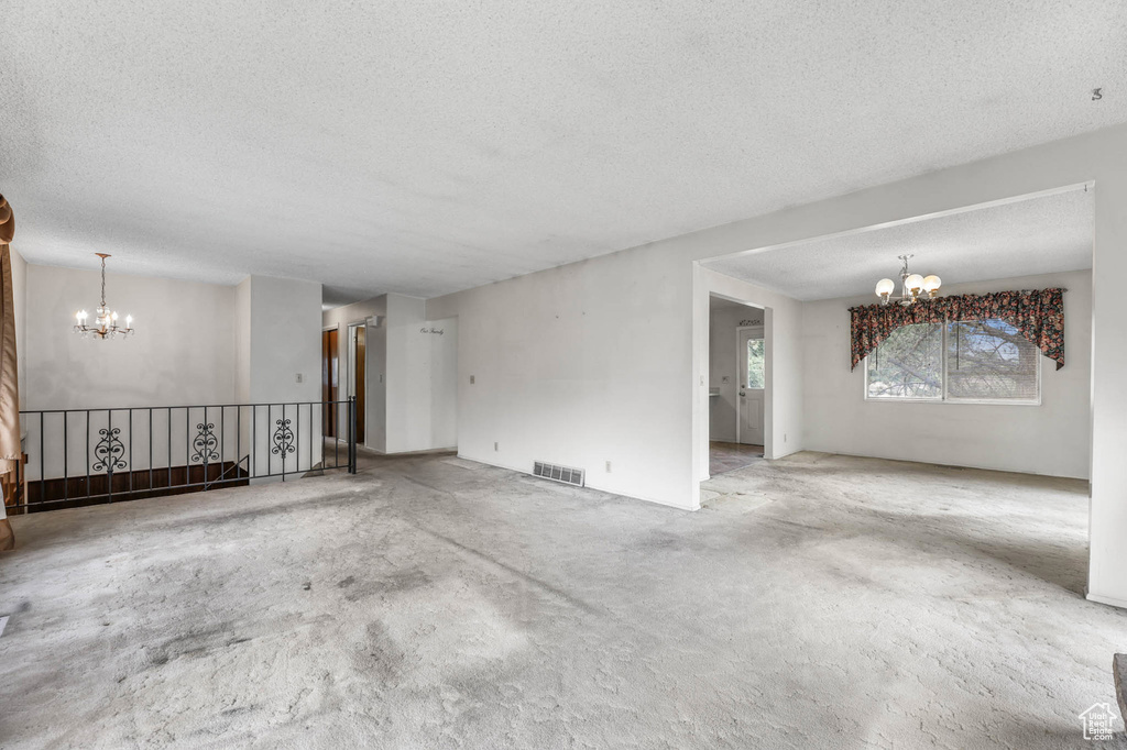 Unfurnished living room with a chandelier, a textured ceiling, and carpet