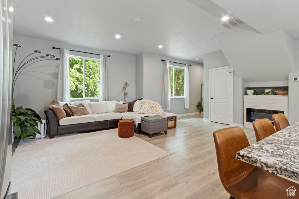 Living area with light wood-style flooring, a glass covered fireplace, healthy amount of natural light, and recessed lighting