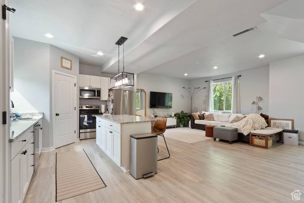 Kitchen featuring stainless steel appliances, light wood-style floors, a center island, a breakfast bar area, and white cabinets