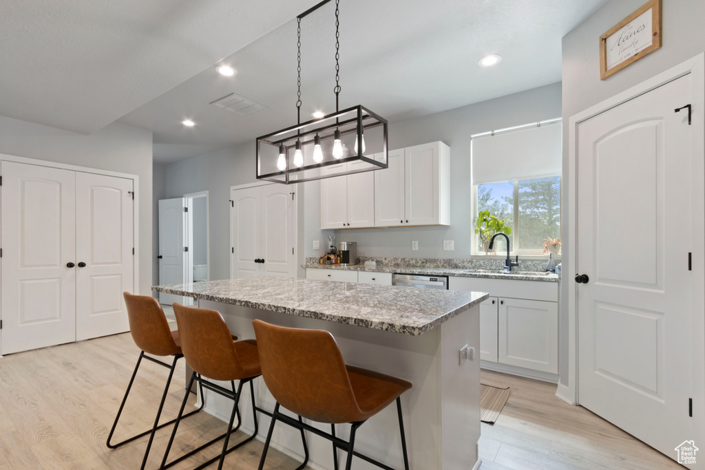 Kitchen featuring a center island, light wood finished floors, recessed lighting, light stone counters, and a breakfast bar area