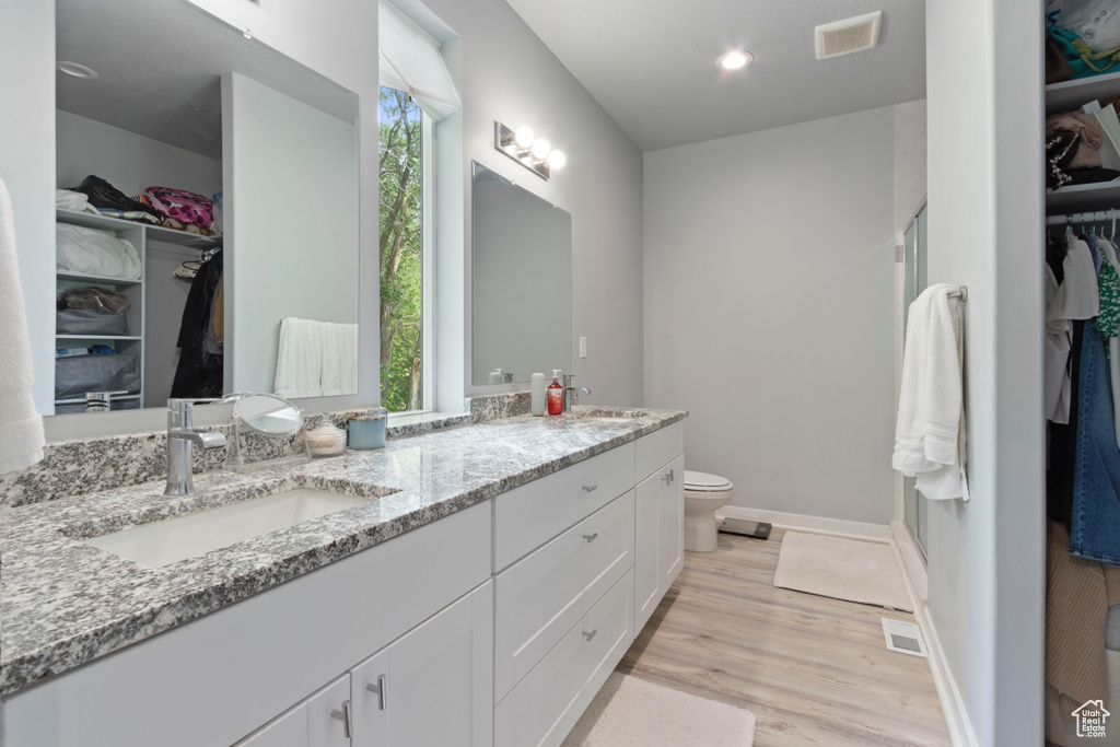 Bathroom featuring double vanity, wood finished floors, a spacious closet, and plenty of natural light