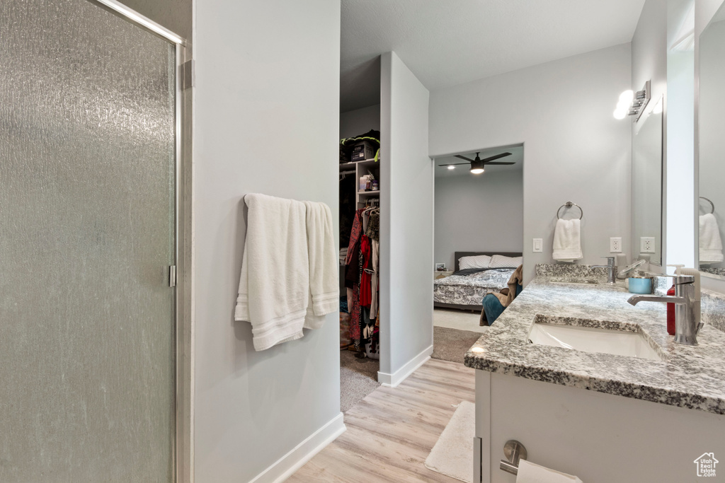 Bathroom featuring a shower stall, wood finished floors, ceiling fan, double vanity, and a walk in closet
