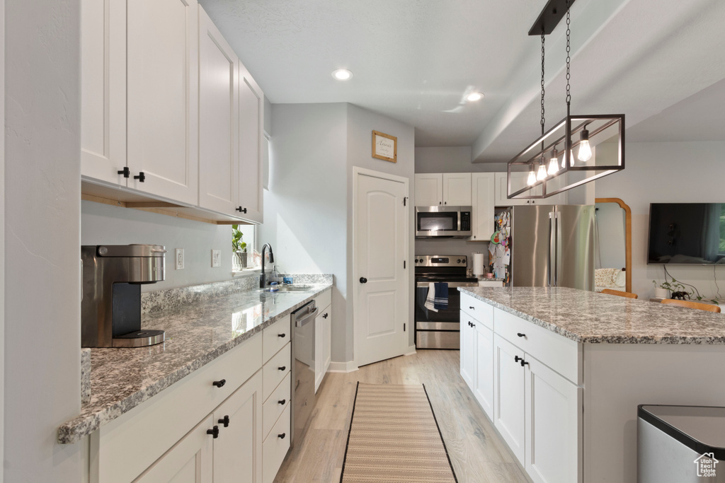 Kitchen with appliances with stainless steel finishes, light wood-style floors, white cabinets, light stone counters, and recessed lighting