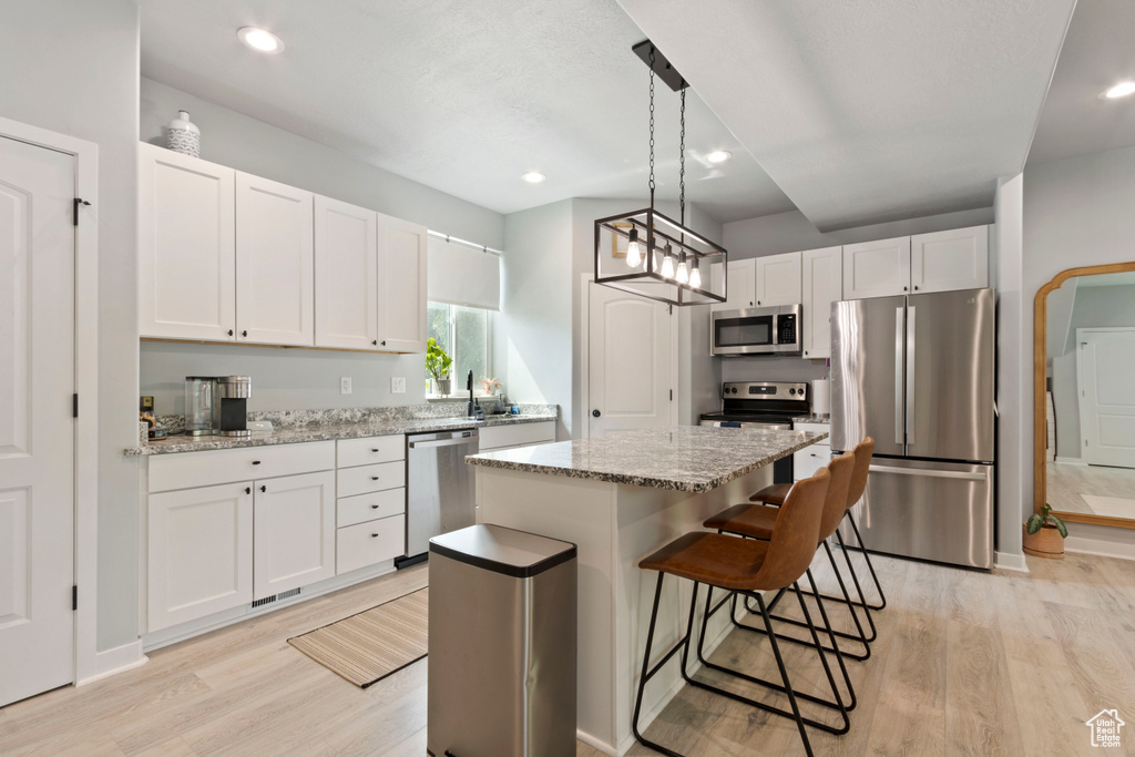 Kitchen featuring appliances with stainless steel finishes, light wood-style floors, a center island, white cabinets, and recessed lighting