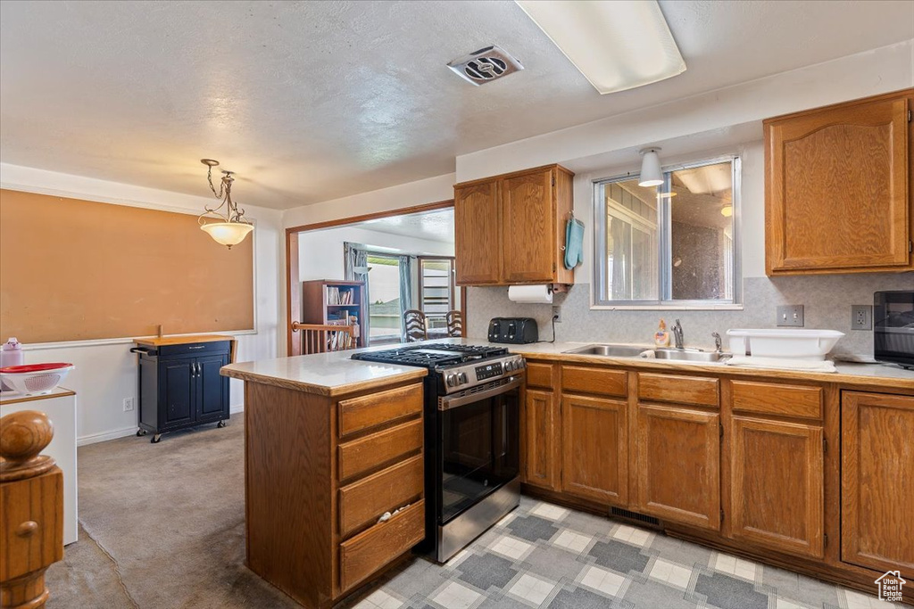 Kitchen with stainless steel gas stove, brown cabinets, a peninsula, light countertops, and light colored carpet
