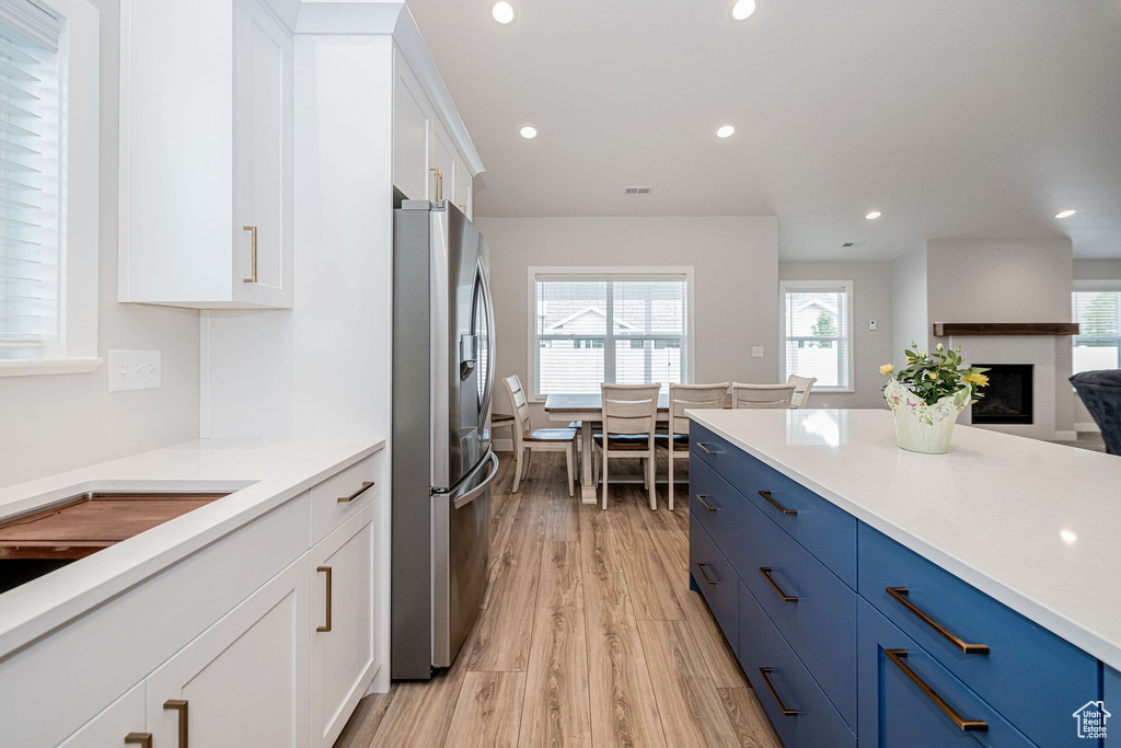 Kitchen featuring stainless steel refrigerator with ice dispenser, blue cabinets, light wood-style floors, white cabinetry, and recessed lighting