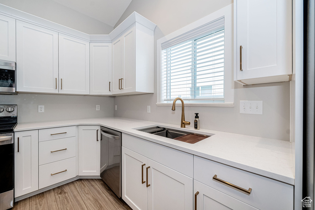 Kitchen with stainless steel appliances, white cabinetry, light countertops, light wood-style flooring, and vaulted ceiling