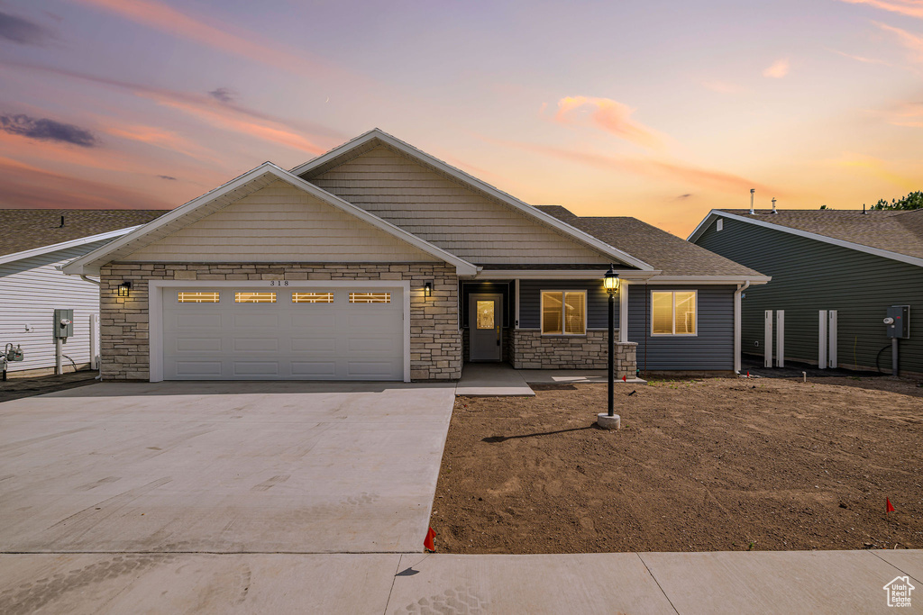 View of front of home featuring driveway, stone siding, a garage, and roof with shingles