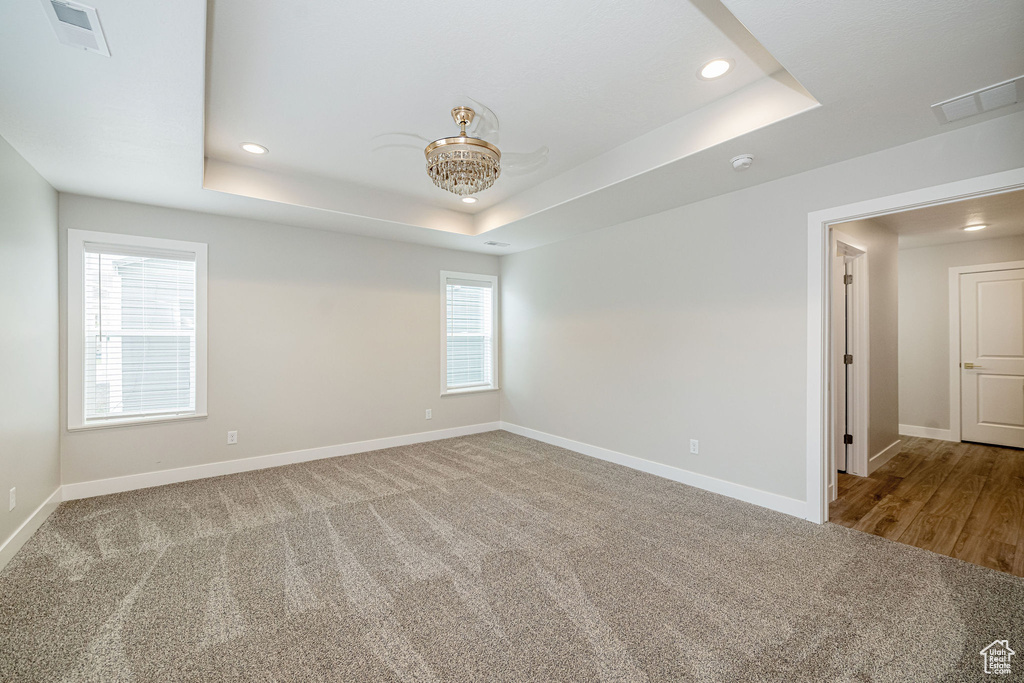 Carpeted empty room with a raised ceiling, recessed lighting, and a chandelier