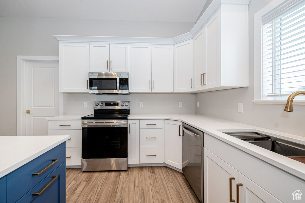 Kitchen with stainless steel appliances, blue cabinetry, light countertops, and white cabinetry