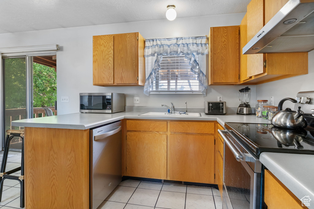 Kitchen with under cabinet range hood, stainless steel appliances, a peninsula, light tile patterned floors, and light countertops