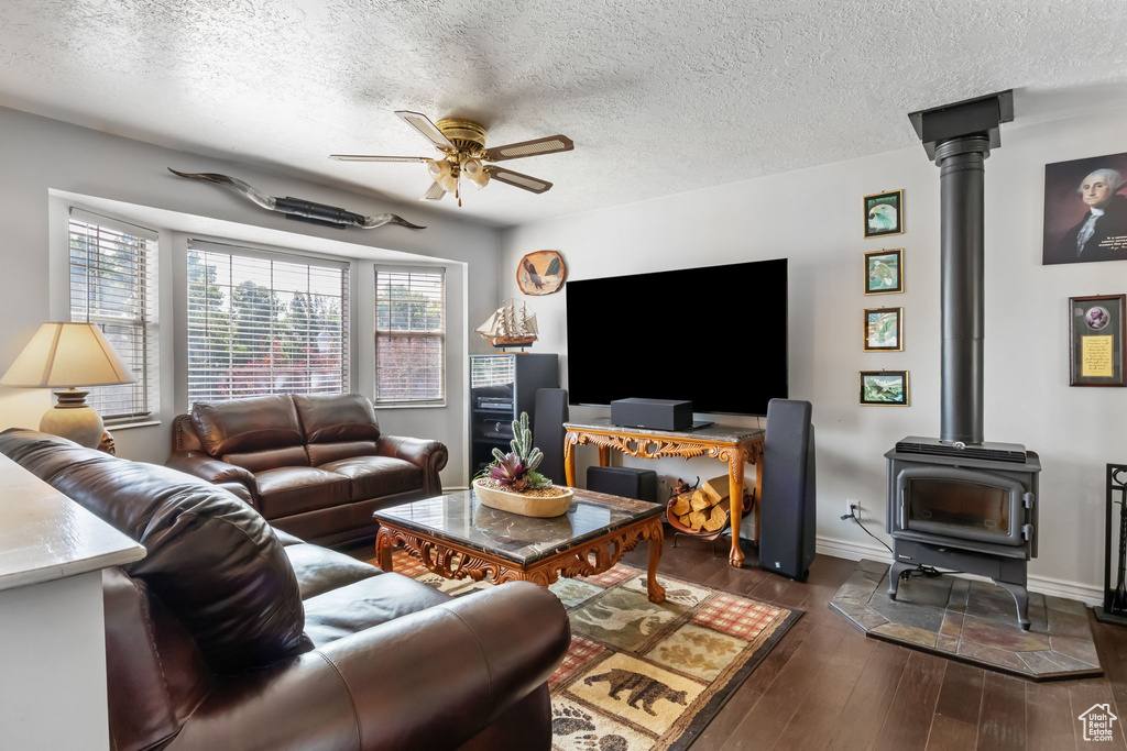Living room with ceiling fan, a textured ceiling, dark wood-type flooring, and a wood stove