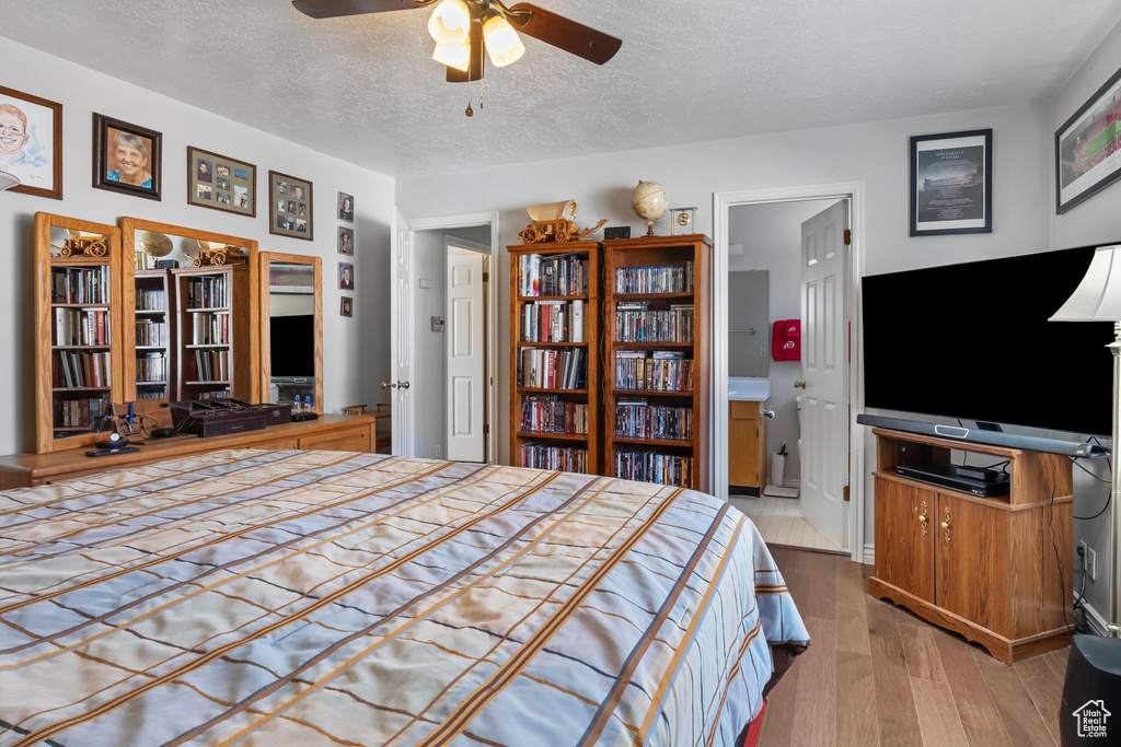 Bedroom featuring wood finished floors, a textured ceiling, a ceiling fan, and ensuite bath