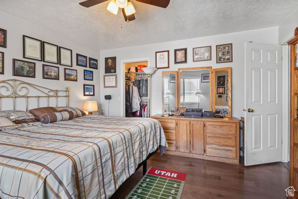 Bedroom featuring a textured ceiling, a spacious closet, dark wood finished floors, a closet, and ceiling fan