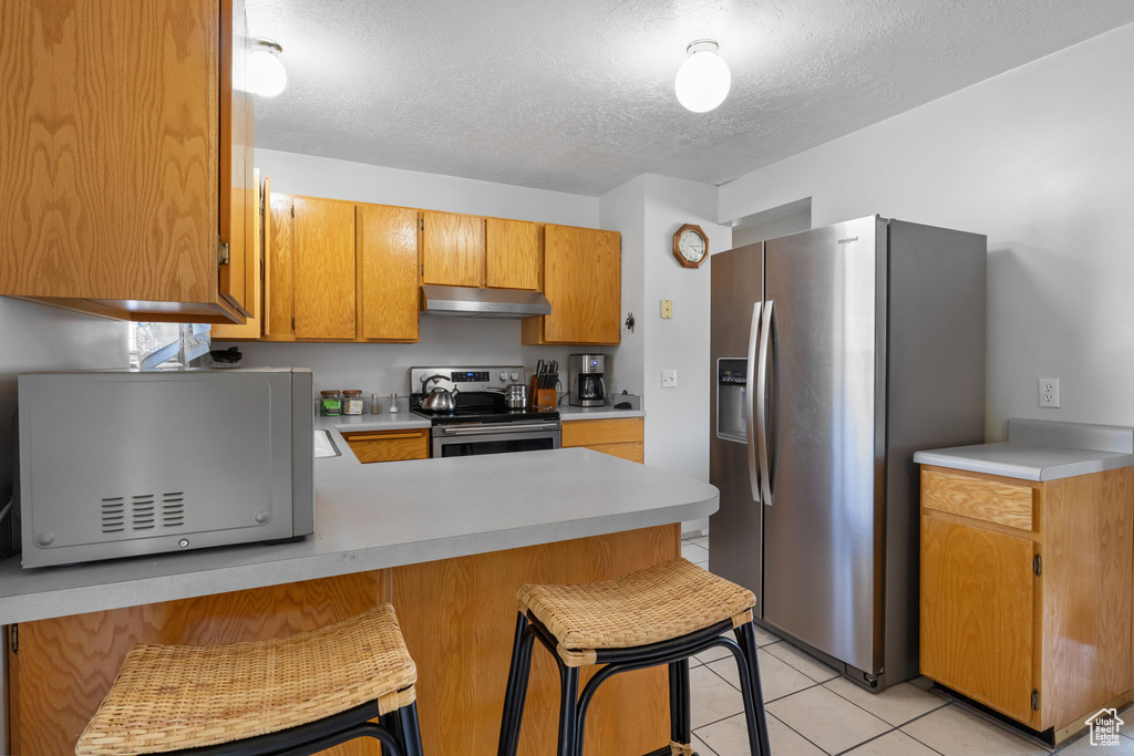 Kitchen with stainless steel appliances, under cabinet range hood, light countertops, a peninsula, and a textured ceiling