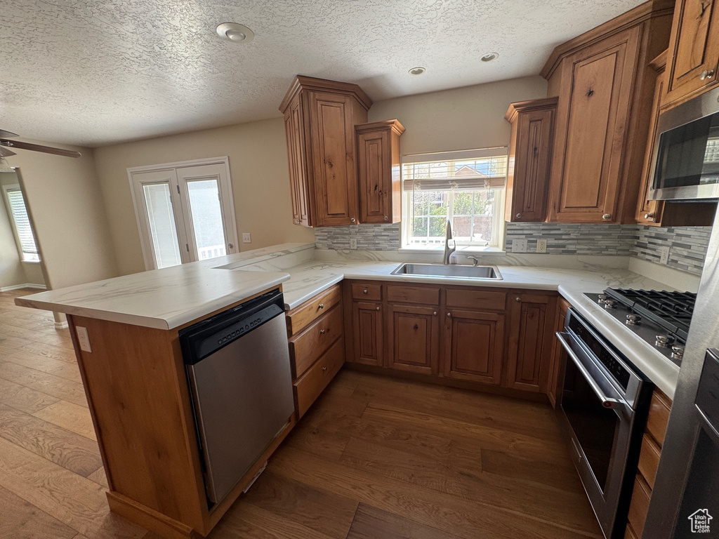 Kitchen with appliances with stainless steel finishes, a peninsula, brown cabinets, dark wood finished floors, and a textured ceiling