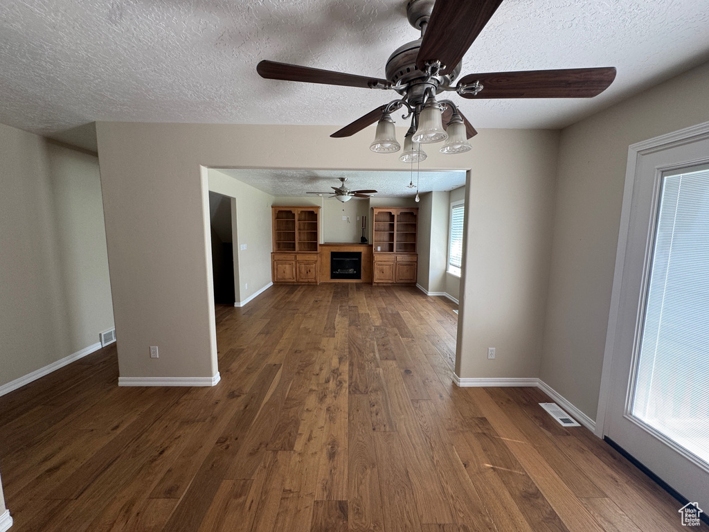 Unfurnished living room with ceiling fan, a textured ceiling, dark wood-style flooring, and a fireplace