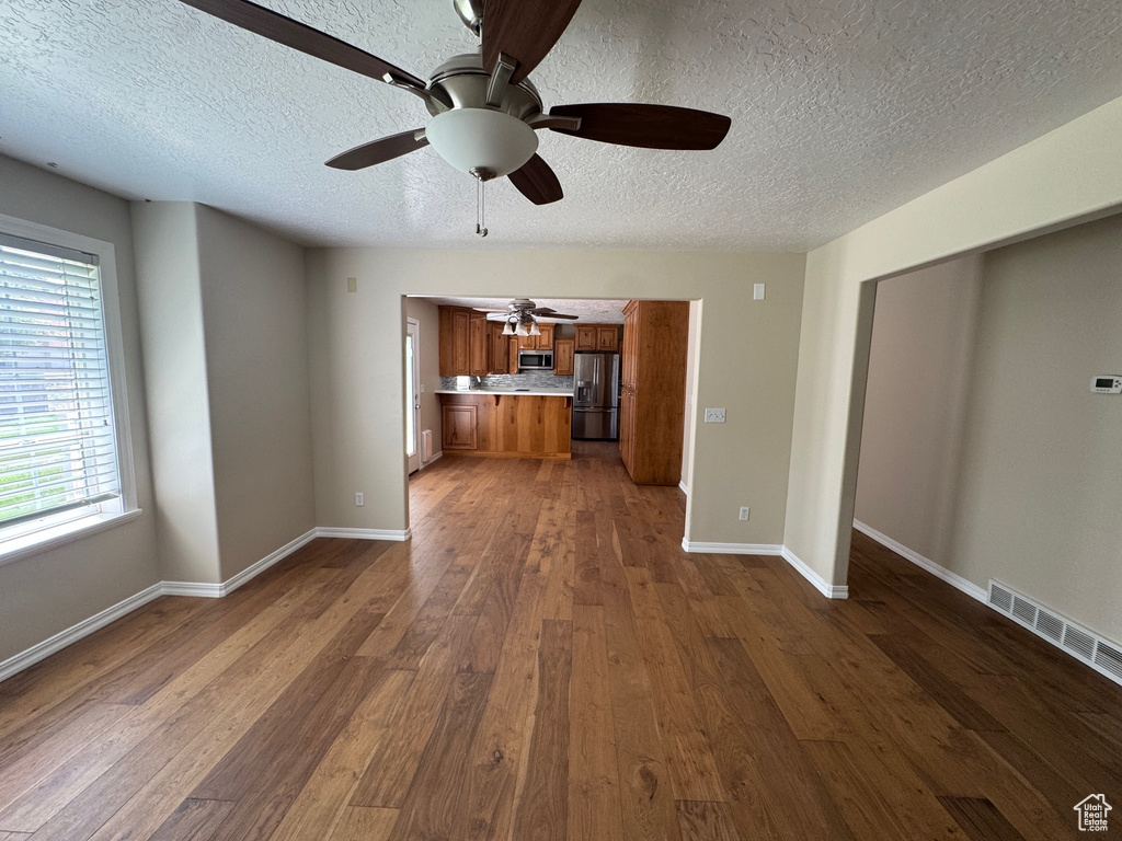 Unfurnished living room with ceiling fan, dark wood finished floors, and a textured ceiling