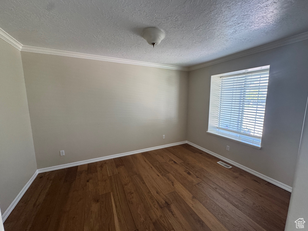 Empty room featuring dark wood-type flooring, a textured ceiling, and ornamental molding