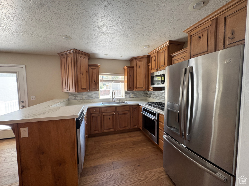 Kitchen featuring stainless steel appliances, hardwood / wood-style flooring, brown cabinetry, light countertops, and tasteful backsplash
