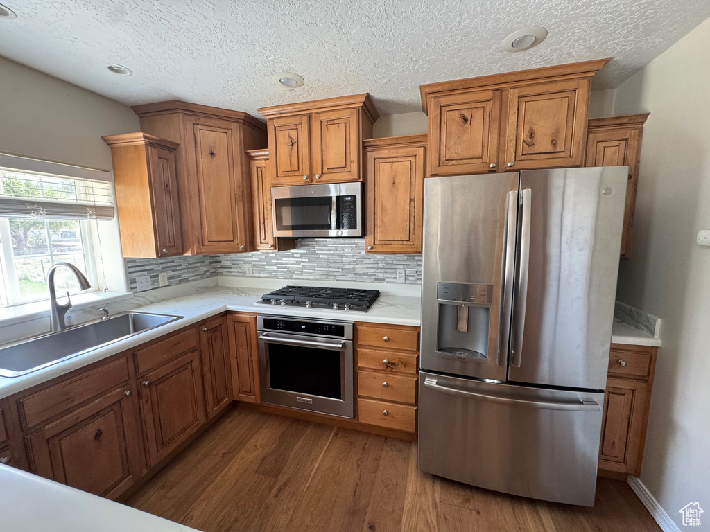 Kitchen with stainless steel appliances, brown cabinets, dark wood-style floors, backsplash, and light countertops
