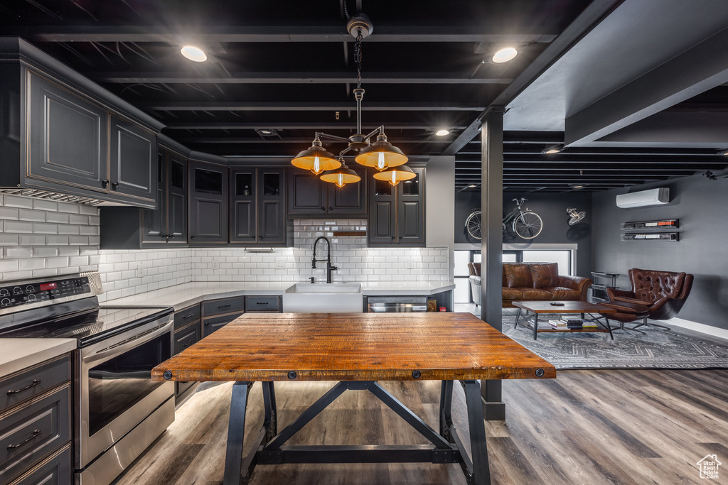 Kitchen with stainless steel electric range, wood finished floors, light countertops, backsplash, and hanging light fixtures