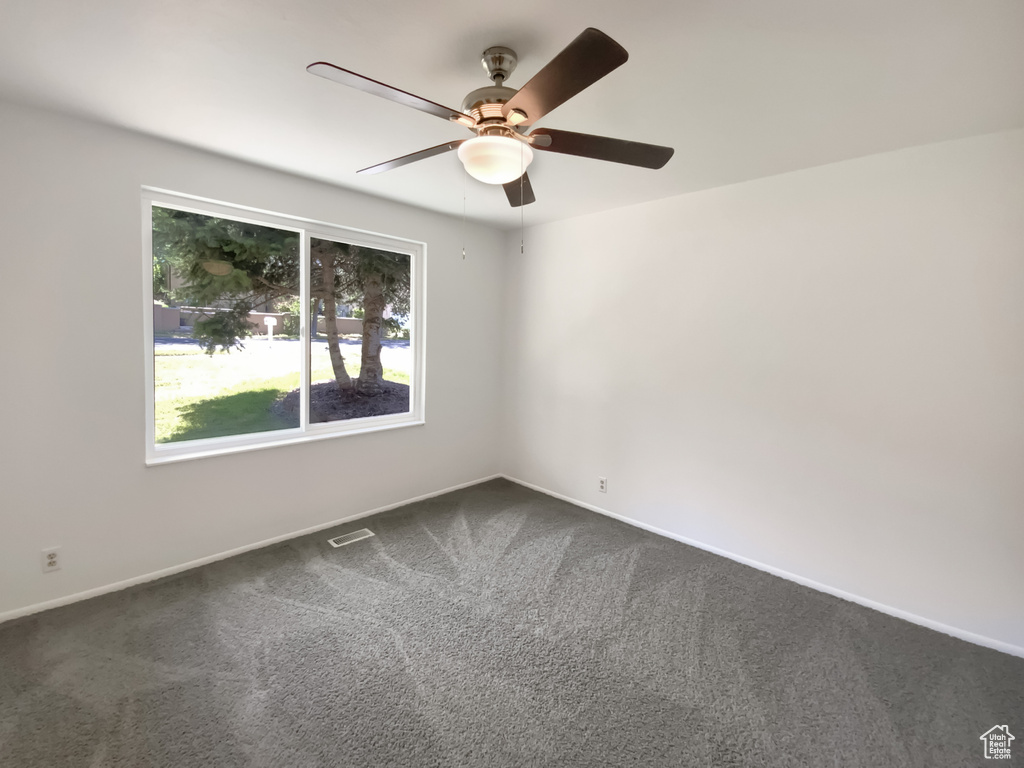 Empty room featuring dark carpet and a ceiling fan