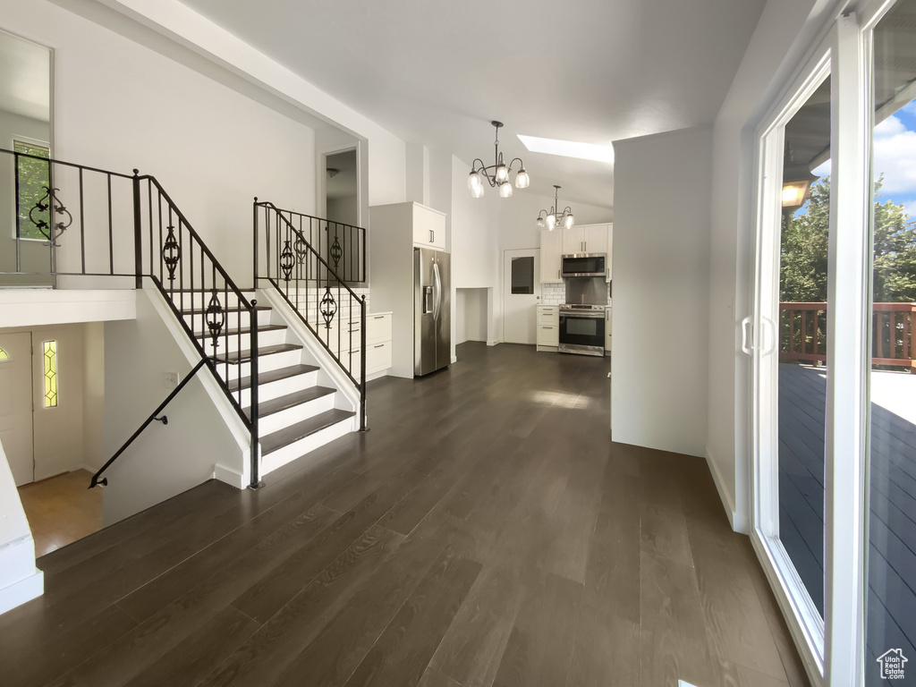 Unfurnished living room with a chandelier, dark wood-style flooring, high vaulted ceiling, and stairs