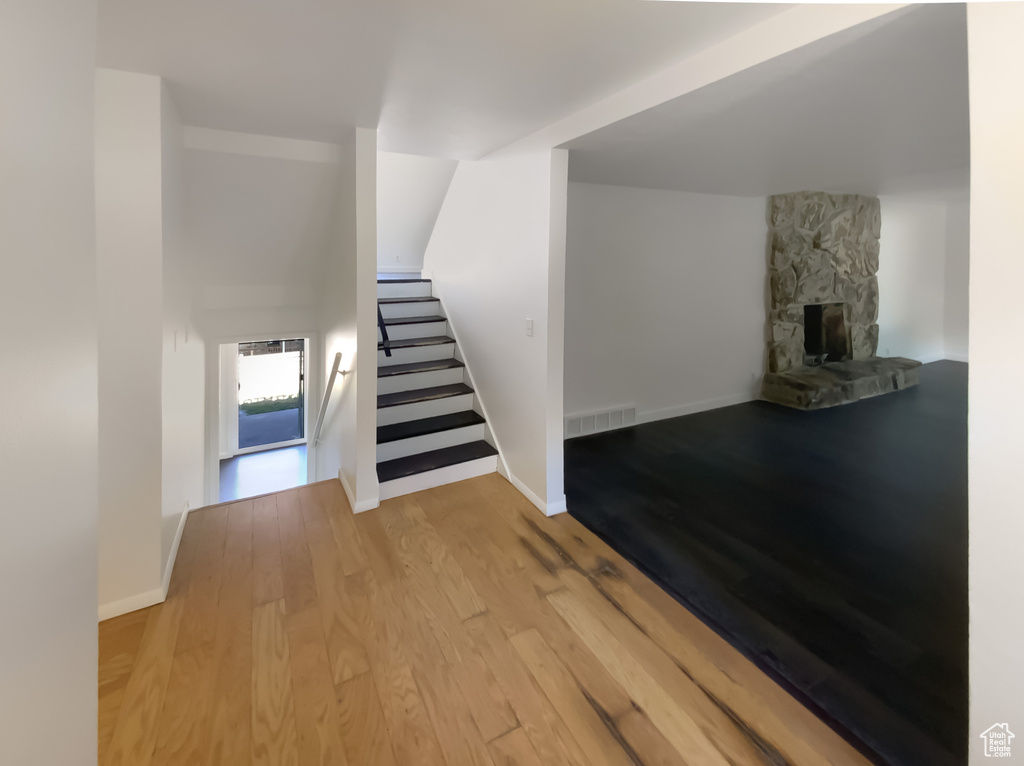 Unfurnished living room with wood finished floors, stairs, and a stone fireplace