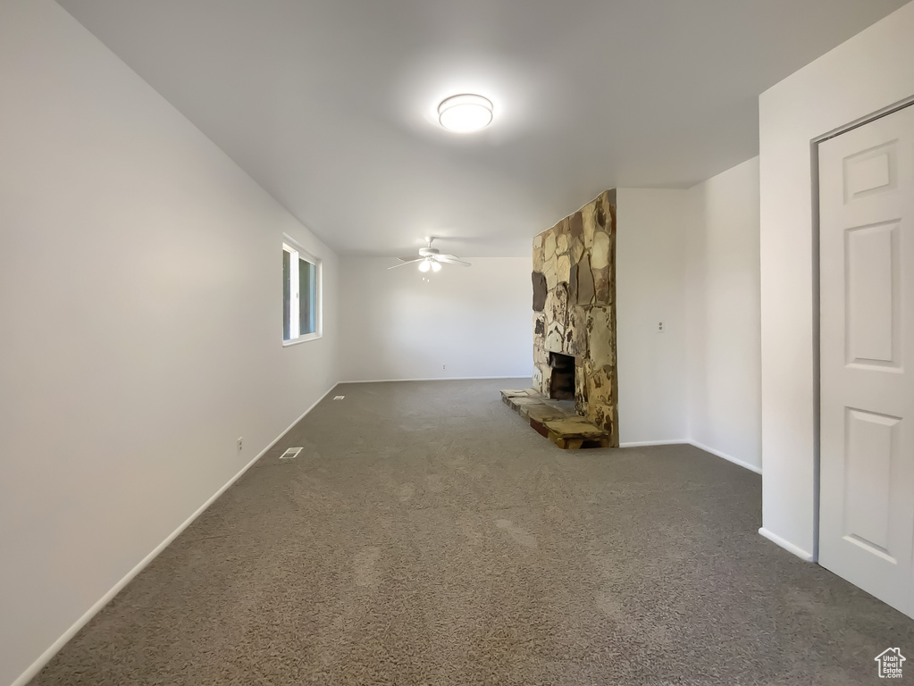 Unfurnished living room featuring a ceiling fan, carpet, and a fireplace