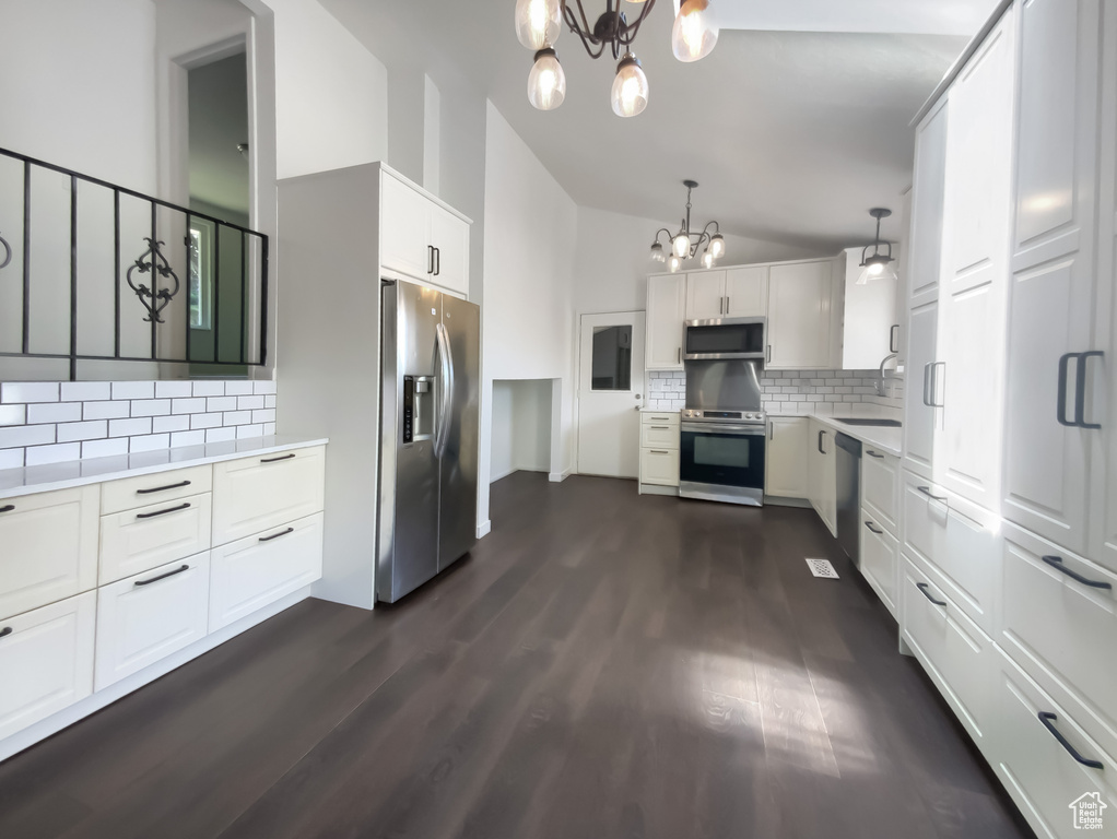 Kitchen with appliances with stainless steel finishes, a chandelier, light countertops, tasteful backsplash, and vaulted ceiling