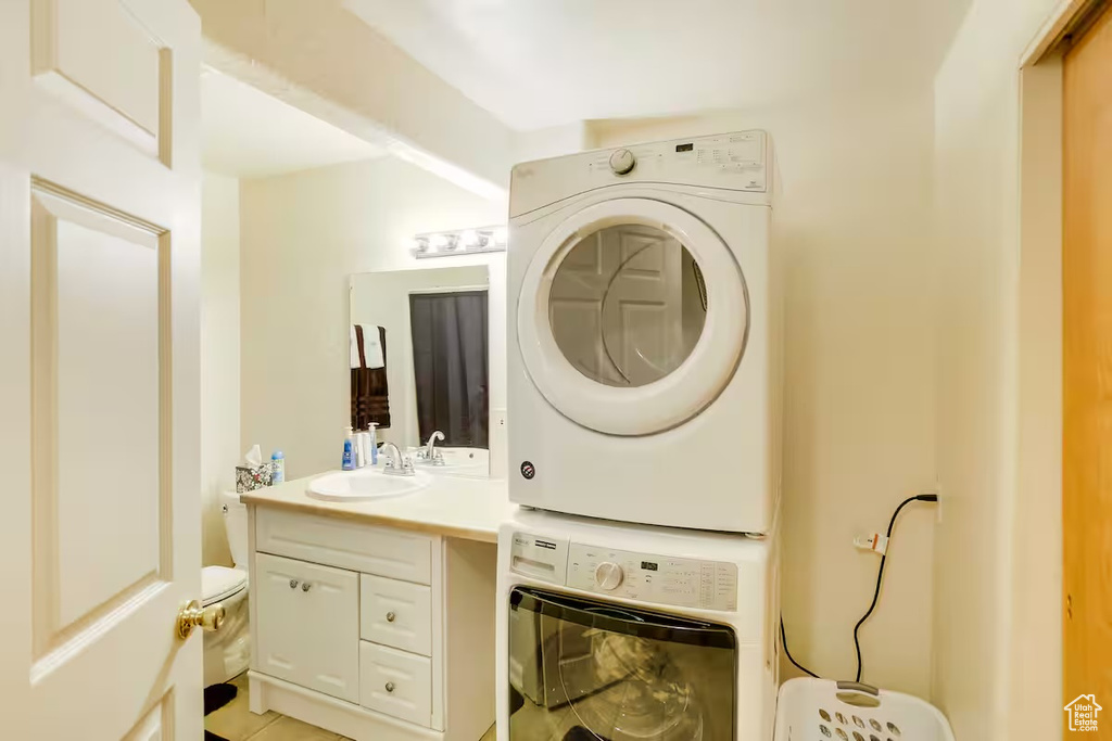 Washroom with stacked washer / drying machine and light tile patterned floors